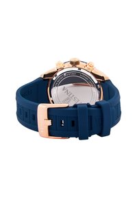 El reloj con correa de goma azul presenta una caja de acero inoxidable de oro rosa, botones de cronógrafo visibles y un fondo de cristal de zafiro.