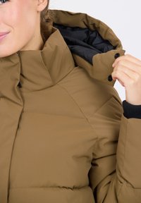 Bruine pufferjack met een hoge kraag, voorzien van een ritssluiting en drukknoopsluiting. Gladde textuur met een doorgestikt ontwerp en zwarte voering.