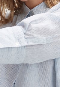 Ljusblå randig skjorta med knapp-ner krage. Har knappar på ärmarna och ett slätt, texturerat tyg.