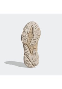 Sneakersula i beige gummi, med vågiga mönster, texturerade sektioner och cirkulära accenter. Flexibelt design med varierade ytor.