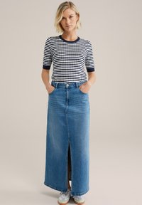 Top de punto de rayas azul marino y blanco con mangas cortas, combinado con una falda larga de mezclilla azul que cuenta con una abertura frontal y bolsillos.