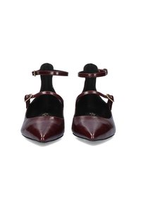 Par de zapatos de cuero burdeos de punta fina con tiras al tobillo y hebilla en tono dorado. Textura suave y diseño aerodinámico. Suela plana.