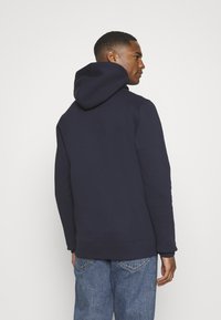 Sudadera de color azul marino con capucha ajustable, hecha de un tejido suave. Presenta un bolsillo tipo canguro y puños y dobladillo acanalados. Combinada con unos jeans de color azul claro.