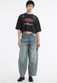 T-shirt noir court avec le logo et les graphiques "GUESS", associé à un jean en denim clair ample avec une coupe droite et des coutures de style utilitaire.