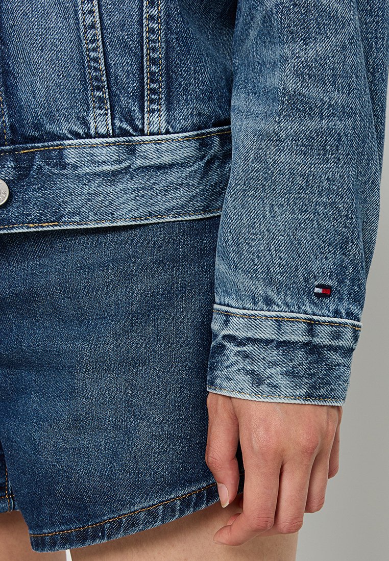 Denimjacke mit einem ausgewaschenen blauen Finish, ausgestattet mit einem Knopfverschluss, verstärkten Nähten und einem kleinen Logostick an der Manschette.