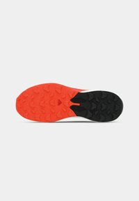 Sko såle med en svart og rød gummisåle med trekantede grepknott, designet for bedre grep og stabilitet.