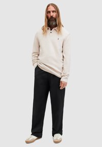Maglione beige chiaro con mezze asole, bottoni neri e una texture sottile. Abbinato a pantaloni neri e sneaker bianche con dettagli beige.