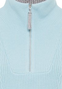 Hellblauer, gestrickter Pullover mit hohem Kragen, der einen Reißverschluss vorne und ein kontrastierendes graues Innenfutter aufweist. Texturiertes Rippdesign über die gesamte Fläche.