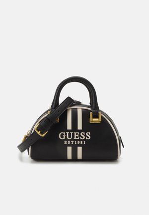 Black semi-circular handbag with two cream vertical stripes, "GUESS EST 1981" logo, black handle, and adjustable strap with gold hardware.