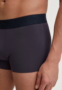 Boxer in stile slip da uomo di colore viola scuro, realizzati in un materiale morbido e elasticizzato. Presentano un elastico in vita di colore blu scuro con incisa la scritta "CALIDA".
