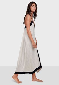 Vestido largo blanco con un patrón sutil, detalles en negro y escote en V. Fabricado con material ligero, cuenta con tirantes finos y un diseño fluido.
