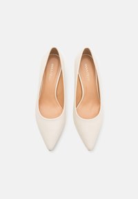 Talons hauts blancs avec un bout pointu et une texture lisse. Les semelles intérieures sont beiges, avec un minimum de marque. Pas d'accents ni de motifs visibles.
