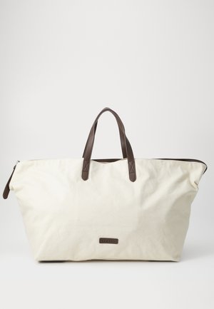 Grand sac en toile beige avec des poignées en cuir brun et une fermeture éclair. Il présente une forme rectangulaire et une étiquette de marque discrète sur le devant.