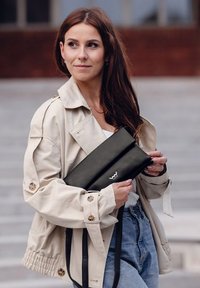 Černá kožená bublina s překládacím designem a embosovaným logem. Nosená s béžovou bundou a modrými džíny, které mají detaily s knoflíky.