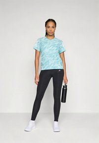 Hele sinine lipsuvärviga funktsionaalne lühikeste varrukatega T-särk valgete detailidega, koos mustade keha järgivate retuusidega. Käes joogipudel.