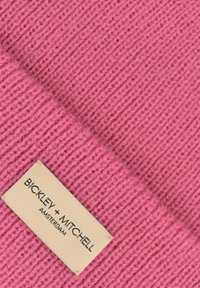 Różowy czapka dziana z żeberkowym wykończeniem. Metka z napisem "BICKLEY + MITCHELL AMSTERDAM" na beżowym tle.