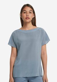 Ljusblå, kortärmad blus med vid halsringning och slät textur. Har lös passform och en flödande design, lämplig för avslappnad användning.