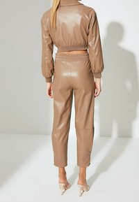 Braune Kunstleder-Cropped-Jacke und passende Hose mit elastischem Bund. Glatte Textur, schmal zulaufendes Bein, dezenten Glanz und eng anliegende Bündchen.