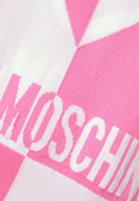Rosa och vit stickad tyg med ett rutigt mönster; stor "MOSCHINO" text i kontrasterande vitt, texturen är mjuk.