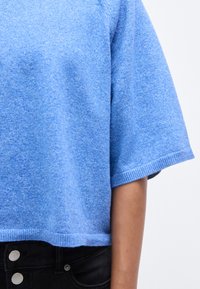 Μπλε cropped πουλόβερ με κοντά μανίκια, κατασκευασμένο από μαλακό ύφασμα, με υφή επιφάνειας και ριμπ τελείωμα, σε συνδυασμό με σκούρο παντελόνι.