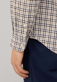 Camisa de botones con un patrón a cuadros en beige, marrón y azul marino. Presenta botones blancos, mangas largas y un dobladillo recto.