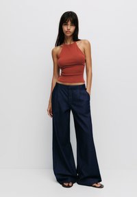 Roestkleurig fitted tanktop gecombineerd met wijde, marineblauwe denim broek. De outfit heeft een minimalistisch ontwerp en soepele texturen.