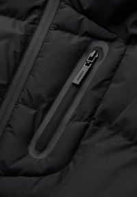 Schwarze gesteppte Jacke mit glänzendem Finish, ausgestattet mit einer Brusttasche mit Reißverschluss und einem verstellbaren Reißverschlusszug. Texturiertes Gewebe mit Steppmuster.