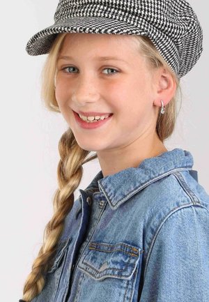 Schwarz-weiße Hahnentritt-Mütze, Jeansjacke mit Knopfverschluss, hellblonder Zopf und kleine glitzernde Ohrringe.