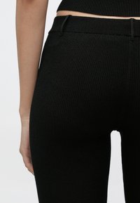 Čierne rebrované legíny s vysokým pásom a bezšvovým dizajnom. Textúra látky je mäkká a elastická, čo zvyšuje pohodlie a priliehavý strih.