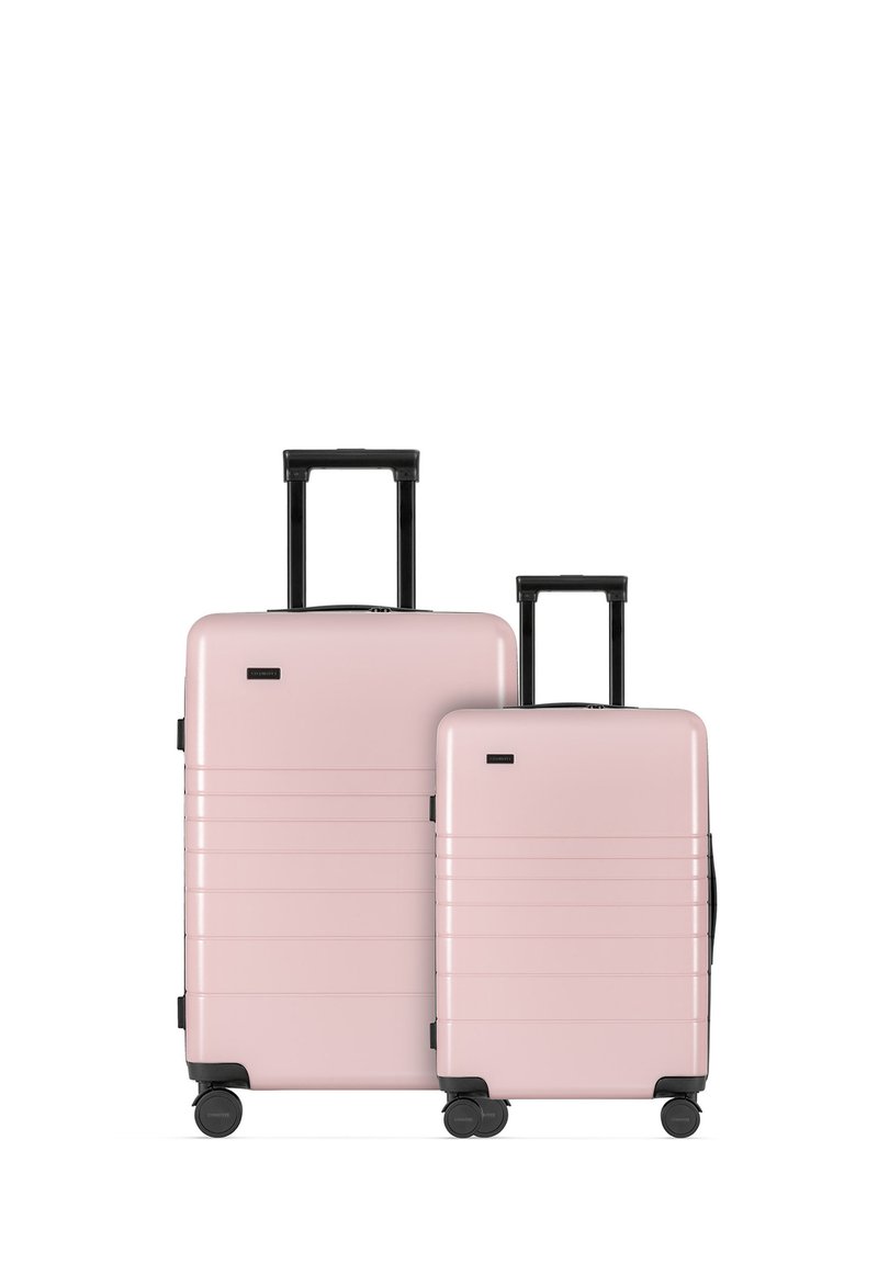 Set of two hard-shell suitcases in pastel pink with black accents, featuring horizontal grooves, extendable handles, and four wheels each.