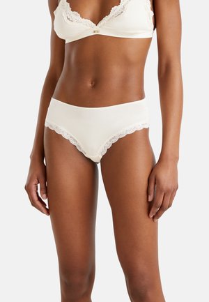 Beżowa bielizna z koronkową lamówką o umiarkowanym kroju, wykonana z gładkiego materiału z falistym brzegiem, o miękkiej, delikatnej fakturze.