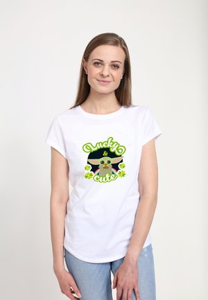 Bílá bavlněná tričko s barevným grafickým designem, na kterém je kreslená postavička, zeleným textem "Lucky & cute" a akcenty trojlístku.