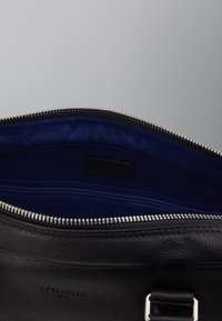 Intérieur d'un sac en cuir noir, avec un revêtement en tissu bleu, une poche zippée et une finition de zip lisse.