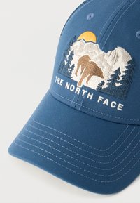 Μπλε καπέλο μπέιζμπολ με κεντημένο βουνό, ήλιο, αρκούδα, δέντρα και το κείμενο «THE NORTH FACE» στο μπροστινό πάνελ.