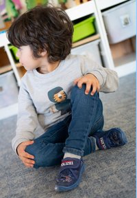 Blauwe kinderschoenen met een autontwerp en de tekst "POLIZEI", gedragen met een spijkerbroek en een lichtgrijze sweatshirt met een tijger.