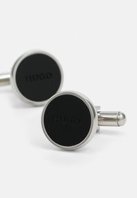 Boutons de manchette ronds avec une finition argentée polie et un centre circulaire noir. Le centre arbore le nom de marque en relief "HUGO."