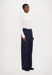 White long-sleeve turtleneck paired with navy wide-leg trousers and black footwear. Trousers feature a smooth texture and high waist.
