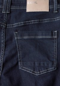 Dunkelblaue Jeans aus Denim mit einer einzelnen Gesäßtasche. Helle Nähte setzen Akzente. Lederetikett mit "CECIL" am Bund befestigt.