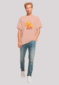 Light pink t-shirt featuring a colorful cartoon dinosaur design, paired with distressed blue jeans and white sneakers.