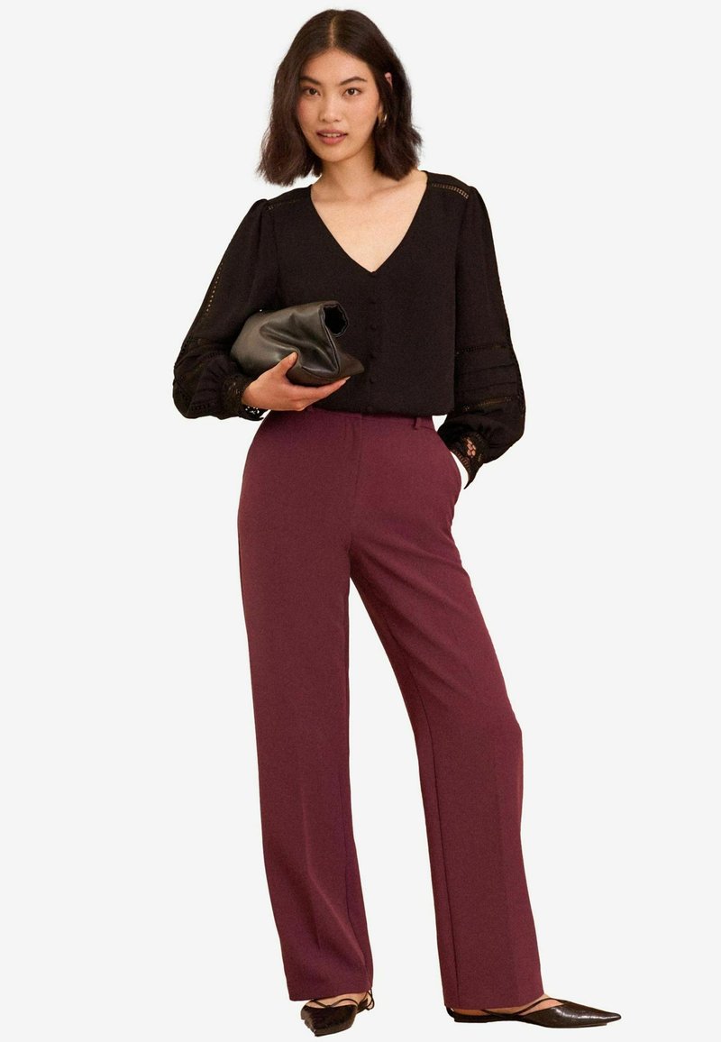 Fekete blúz V-kivágással és csipke díszítéssel, magas derékú bordó, bőszárú nadrággal párosítva. A modellen fekete clutch található.