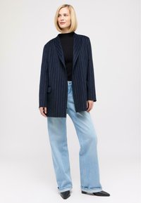 Navy pinstripe oversized blazer over a black turtleneck, paired with light blue wide-leg jeans, and black pointed-toe heels.