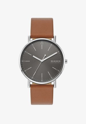 Round Skagen watch with a dark gray dial, silver hour markers, and a brown leather strap. Minimalist design, clean lines, and polished finish.