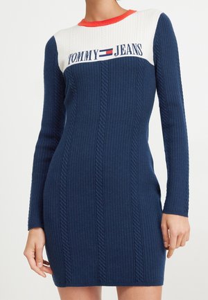 Granatowa sukienka dzianinowa w splot warkoczowy z białym karczkiem, czerwonym dekoltem, długimi rękawami i logo "Tommy Jeans" na piersi.
