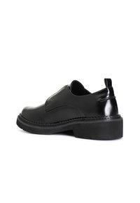 Zapatos negros de piel sin cordones con un acabado brillante, punta redondeada y suela de goma texturizada. Presentan una pequeña pestaña en el talón y detalles de costura.
