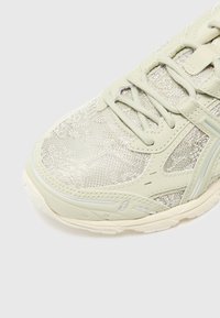 Svetlozelená športová obuv s textúrovaným kovovým sieťovým zvrškom, šnurovaním a masívnou bielou podrážkou. Disponuje reflexnými akcentmi a detailami šitia.