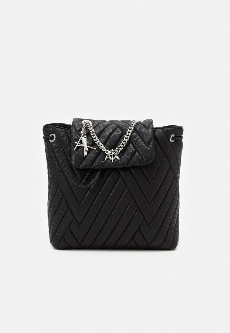 Sac à main noir matelassé avec motif chevron, détail chaîne argentée et breloques en forme de lettres sur le rabat avant, sur un fond blanc uni.