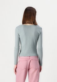 Vaaleansininen ribattu pitkähihaisten toppi pyöreällä pääntiellä, yhdistettynä punavalkoisiin raidallisiin korkeavyötäröisiin housuihin, joissa on rento istuvuus.