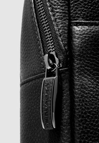 Detail einer schwarzen Ledertasche mit einem Reißverschluss mit Metallzuglasche, strukturierter Oberfläche und sichtbaren Nähten, die Langlebigkeit und Qualität betonen.