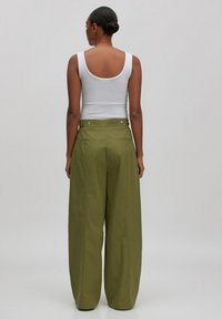 Weißes Tanktop kombiniert mit weitgeschnittenen olivgrünen Hosen. Die Hosen haben eine hohe Taille und Gesäßtaschen, mit subtiler Glanz und Textur.
