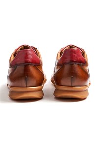 Chaussures en cuir marron avec un accent en cuir rouge au talon, design arrondi, semelle en caoutchouc texturée et coutures détaillées à l'arrière.